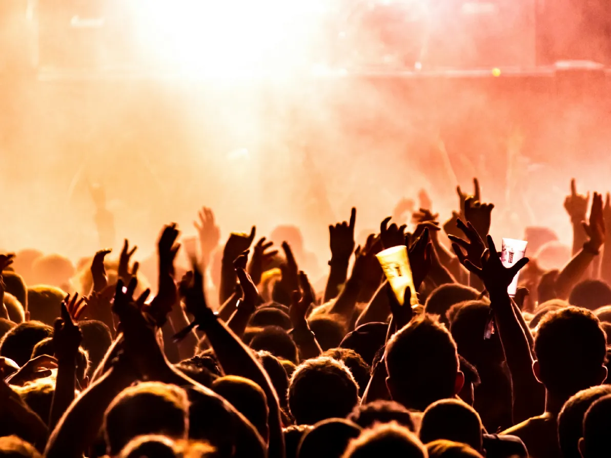 Público con las manos arriba frente a la tarima iluminada durante un concierto